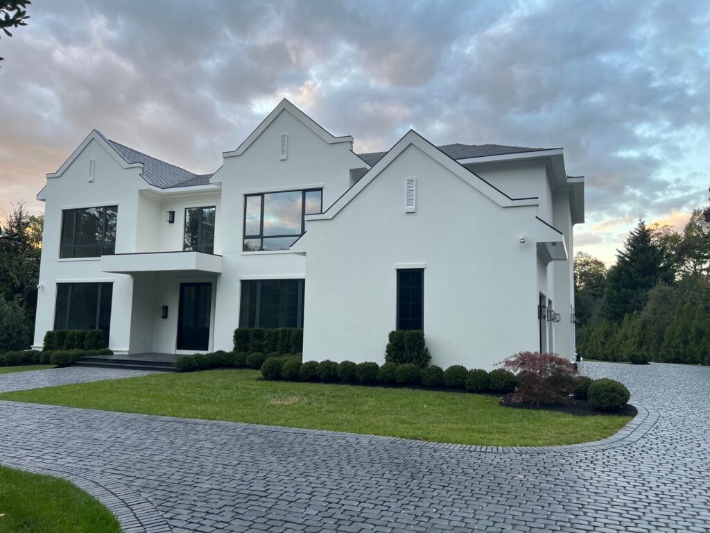 Modern white house with a clean lawn and cobblestone driveway.