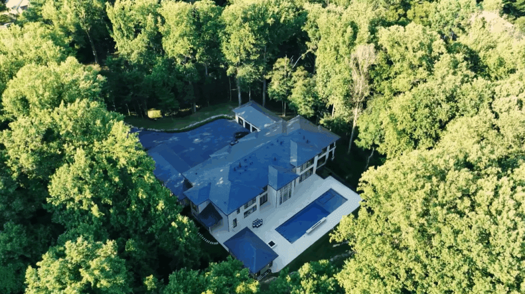 A large modern house surrounded by dense trees with a swimming pool.