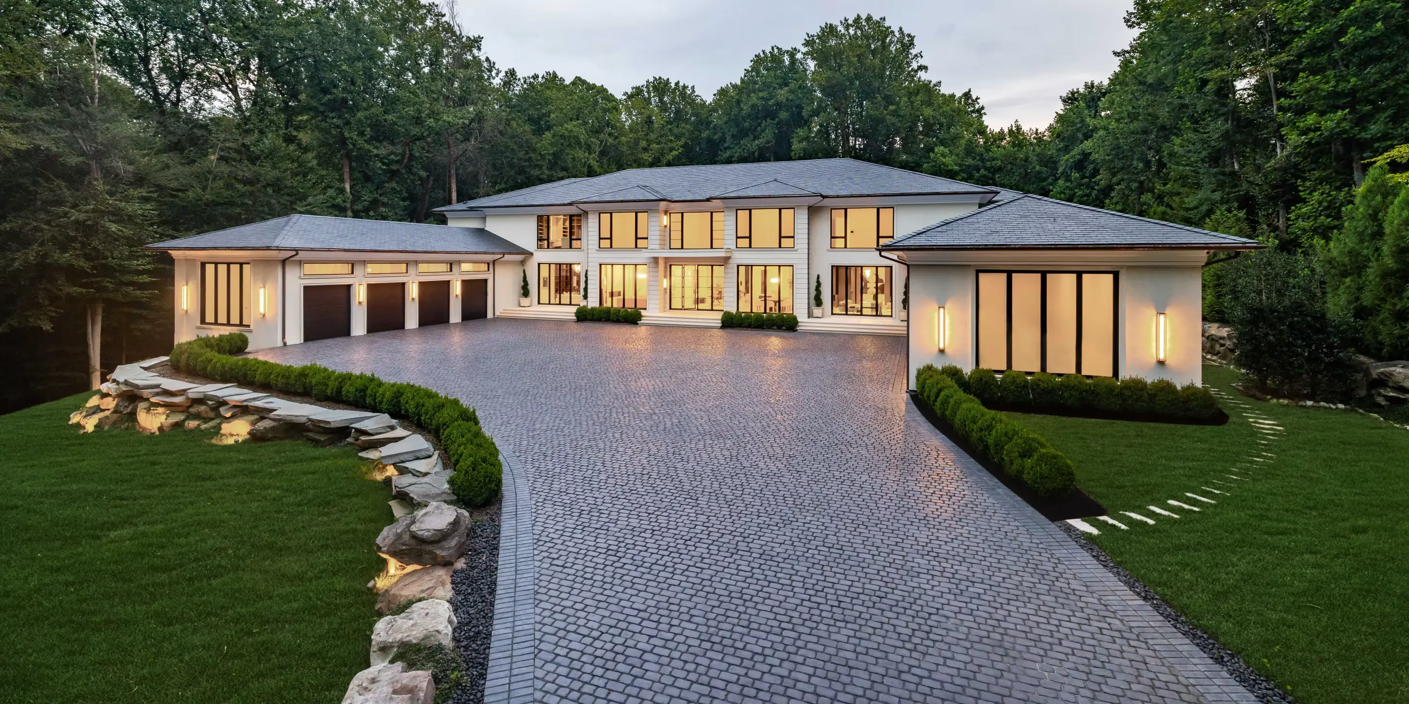 Luxurious modern mansion with expansive driveway and landscaped greenery.