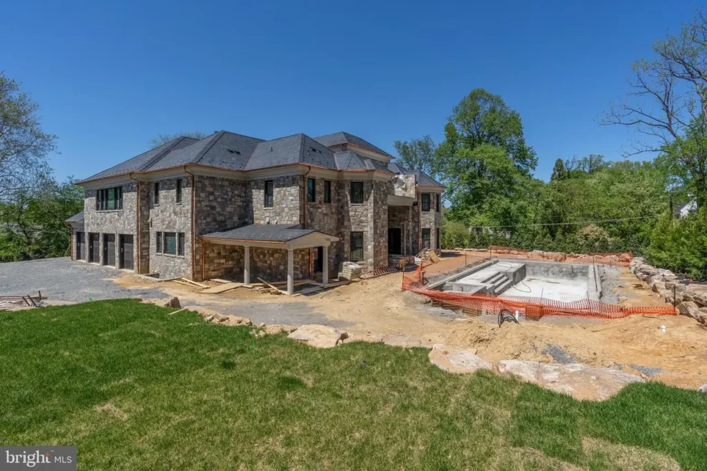 Large stone house with a pool under construction in the backyard.