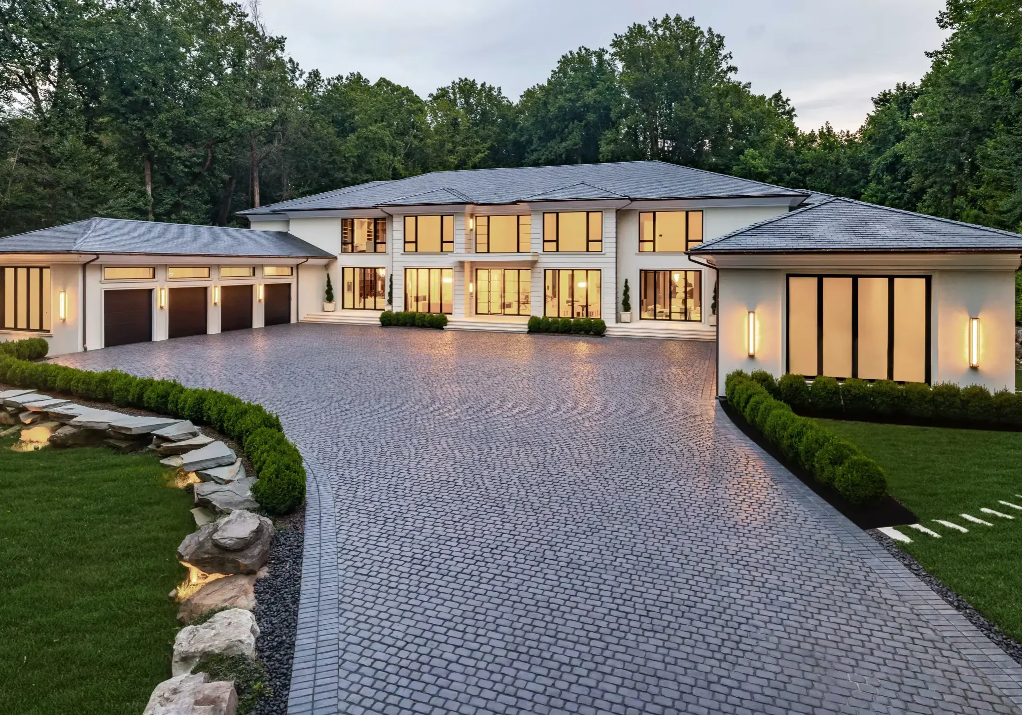 Luxurious modern mansion with expansive driveway and landscaped greenery.